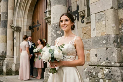 Mariée en robe de satin ivoire devant une église en pierre lors d'un mariage élégant en France